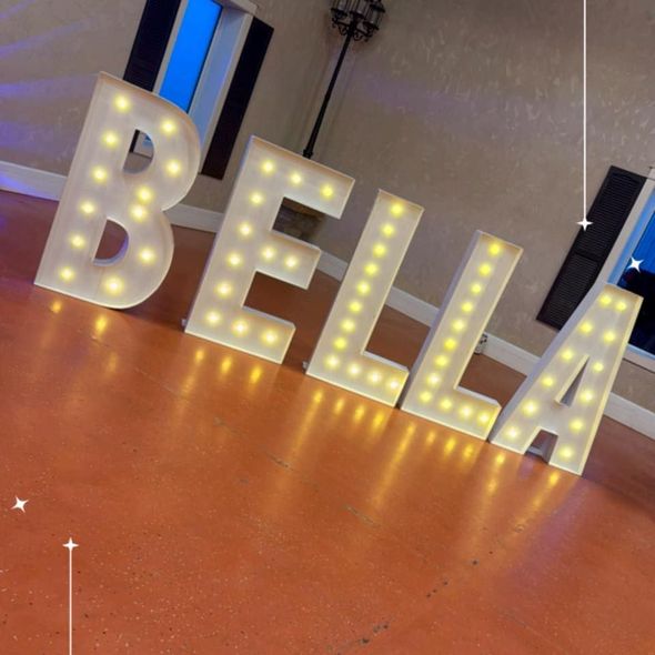 Illuminated white “BELLA” marquee letters on an orange floor indoors