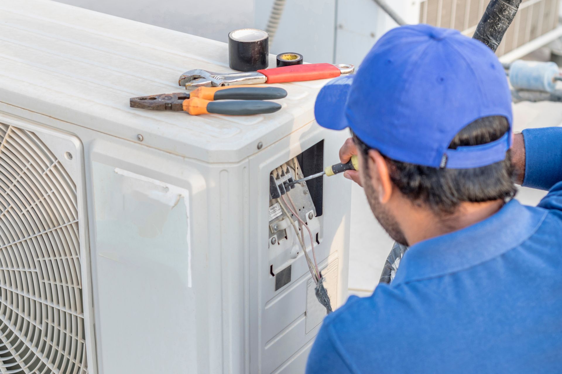 AC Services technician repairing an outdoor air conditioning unit with tools placed on top of the system. AC Services technician repairing an outdoor air conditioning unit with tools placed on top of the system.