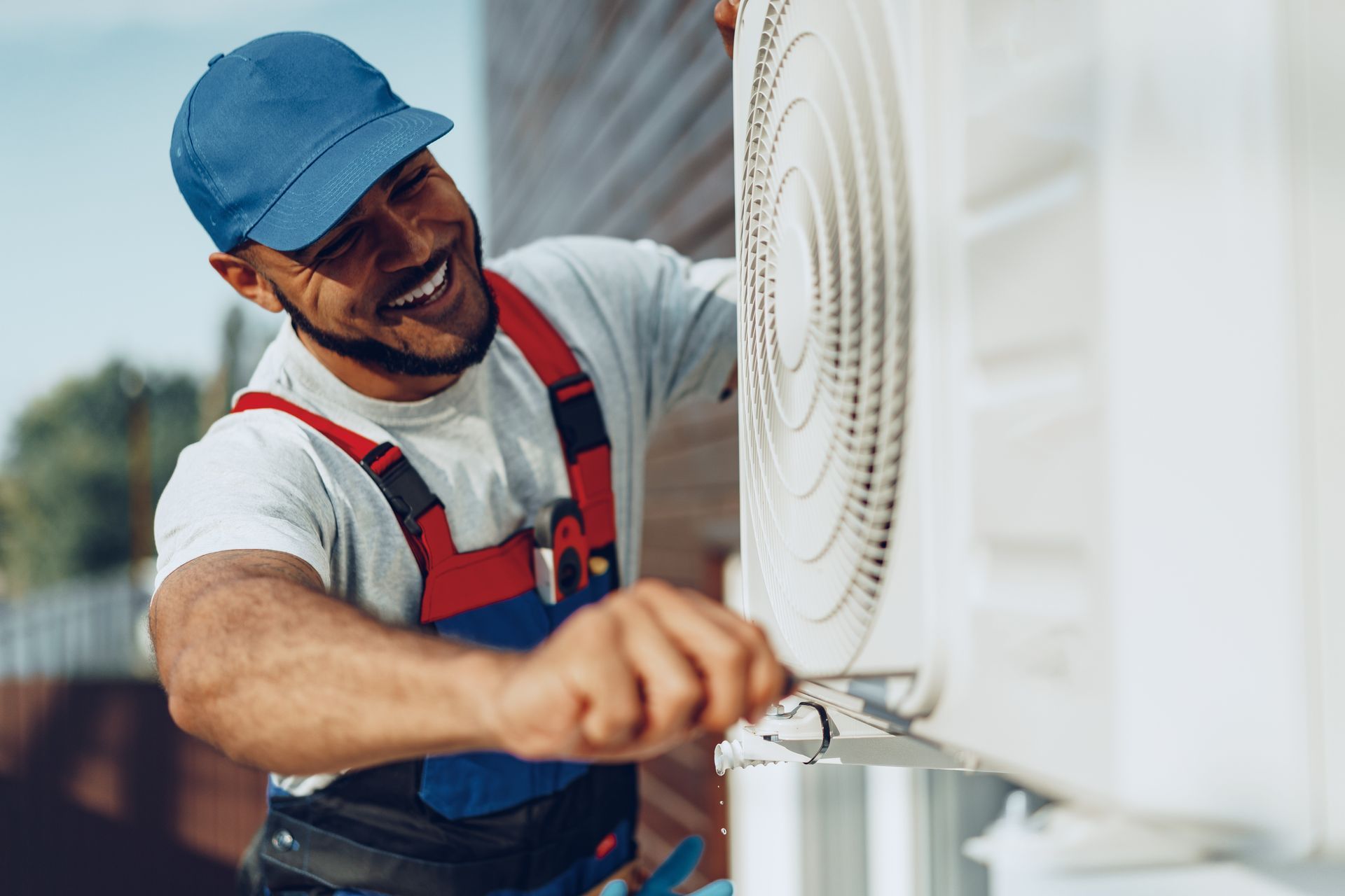 Technician in blue cap and red overalls servicing an outdoor air conditioner unit Technician in blue cap and red overalls servicing an outdoor air conditioner unit