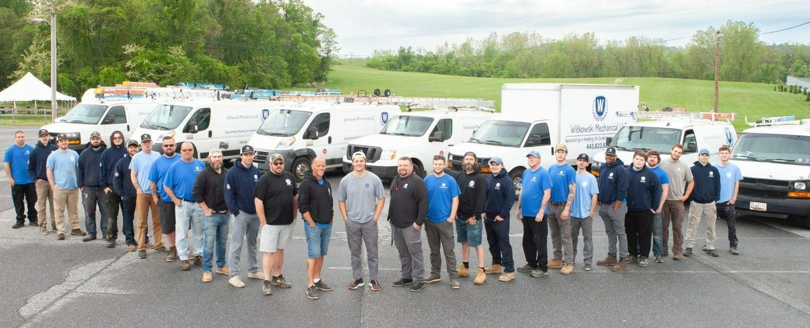 A group of service workers stand in front of their white vans. They are in blue company shirts.