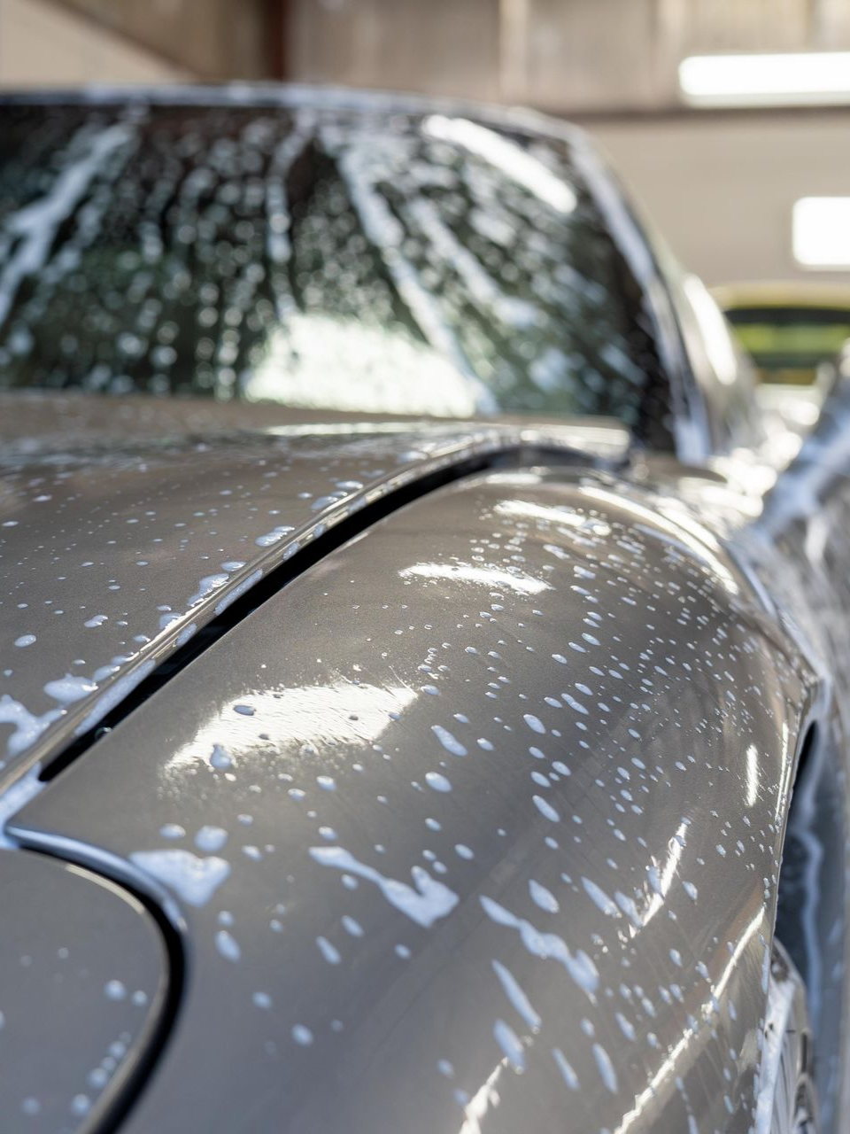 Close-up of a gray car roof and hood covered in water droplets in a parking garage