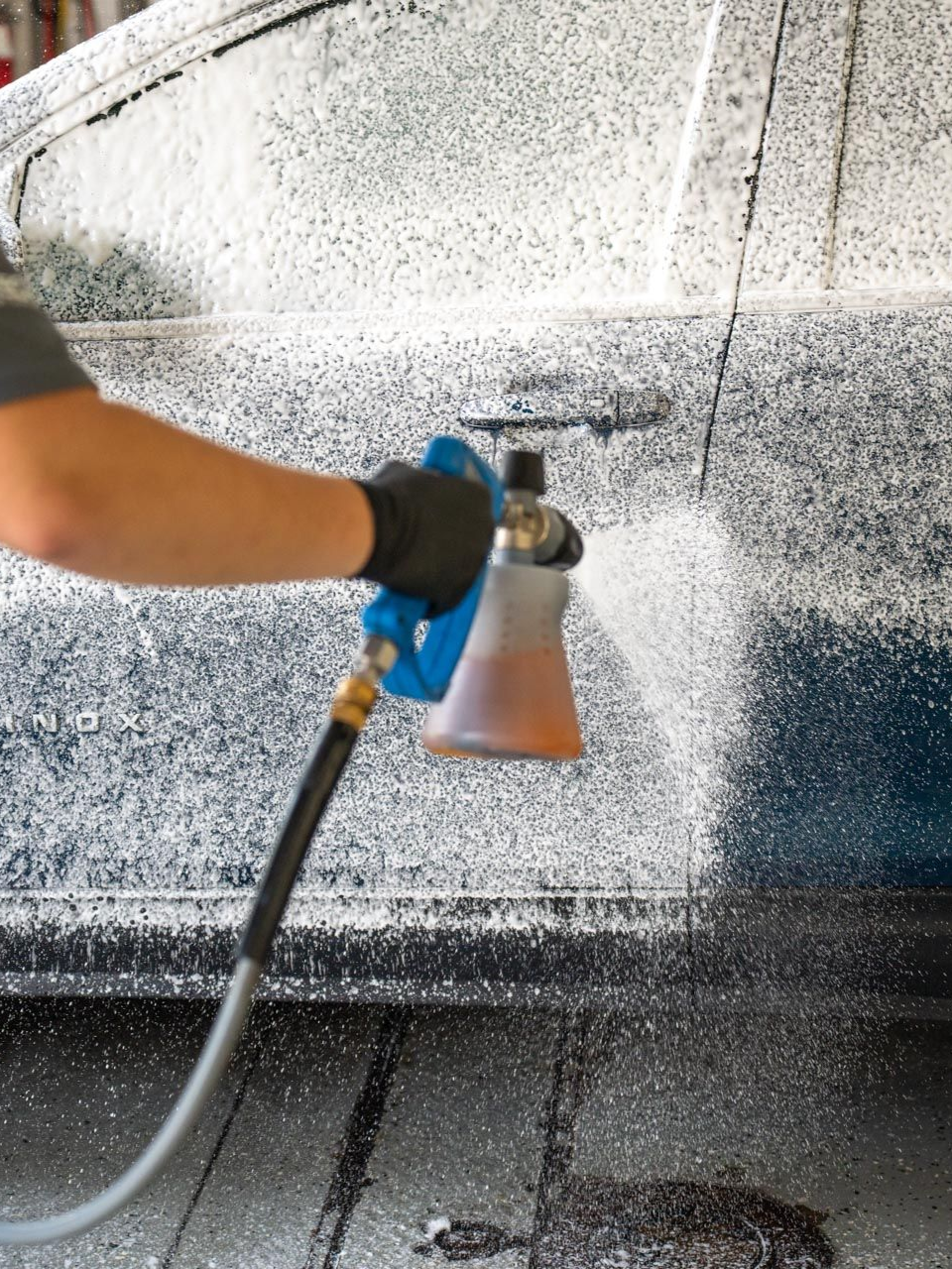 Person spraying cleaning solution with a hose onto a vehicle surface