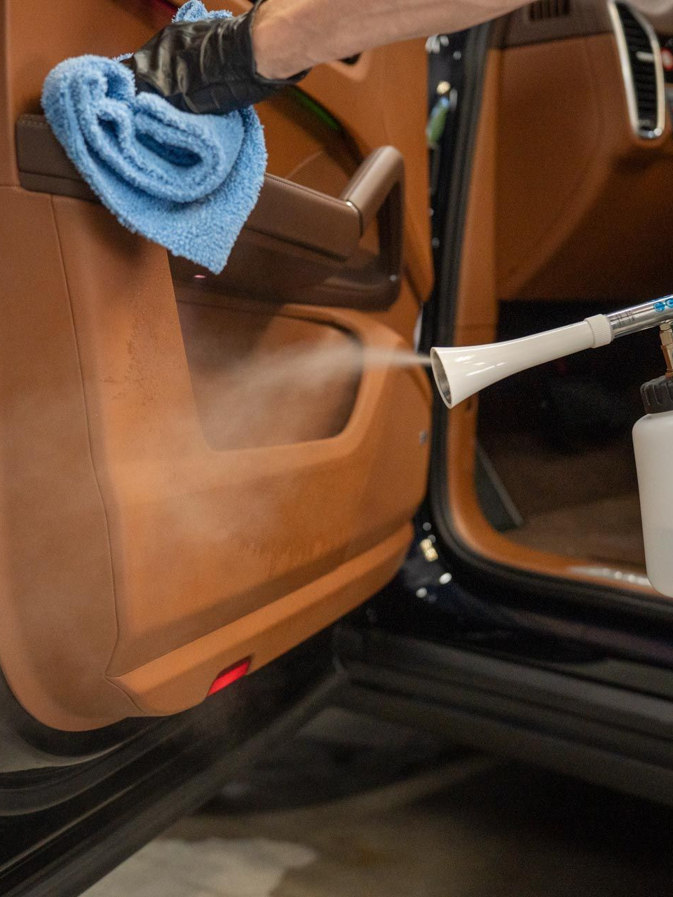 Steam cleaning a tan car interior with a cloth and nozzle