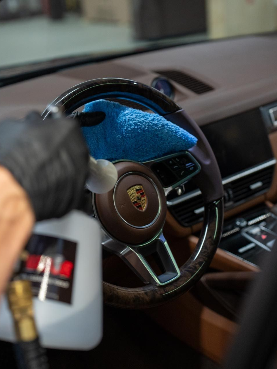 Blue microfiber cleaning a Porsche steering wheel and dashboard inside a luxury car interior
