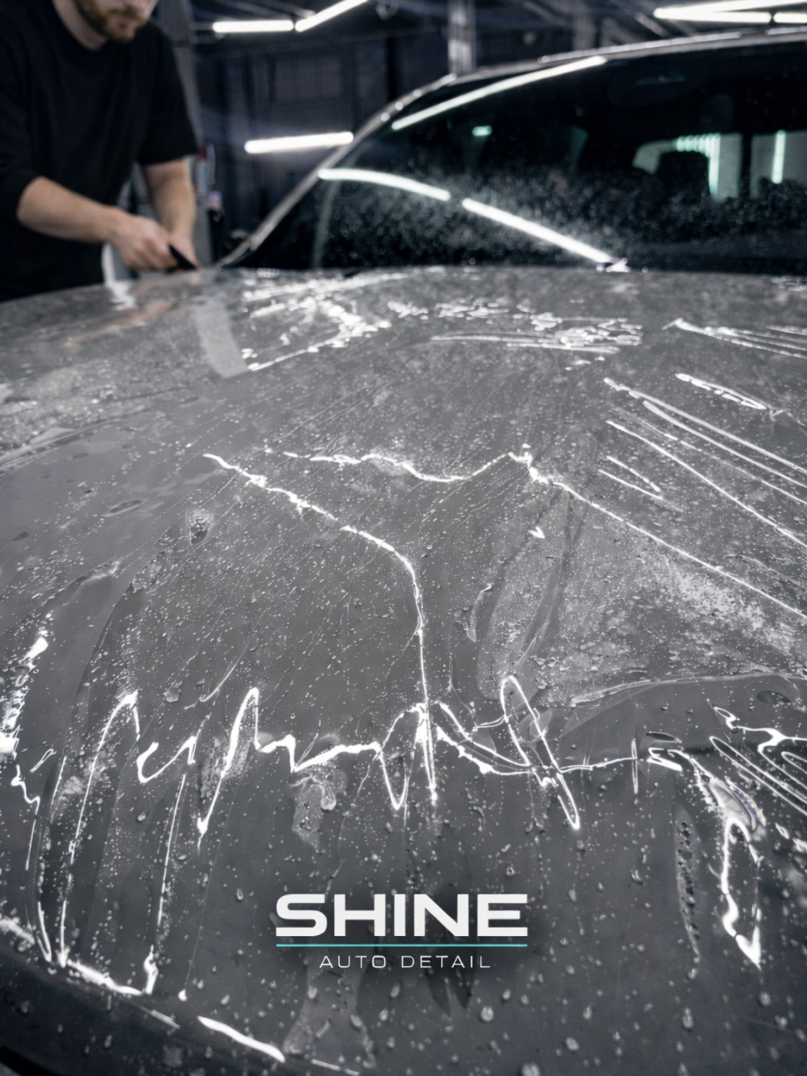 Car hood being washed with foamy soap by a detailer at a car wash, with SHINE logo on the vehicle
