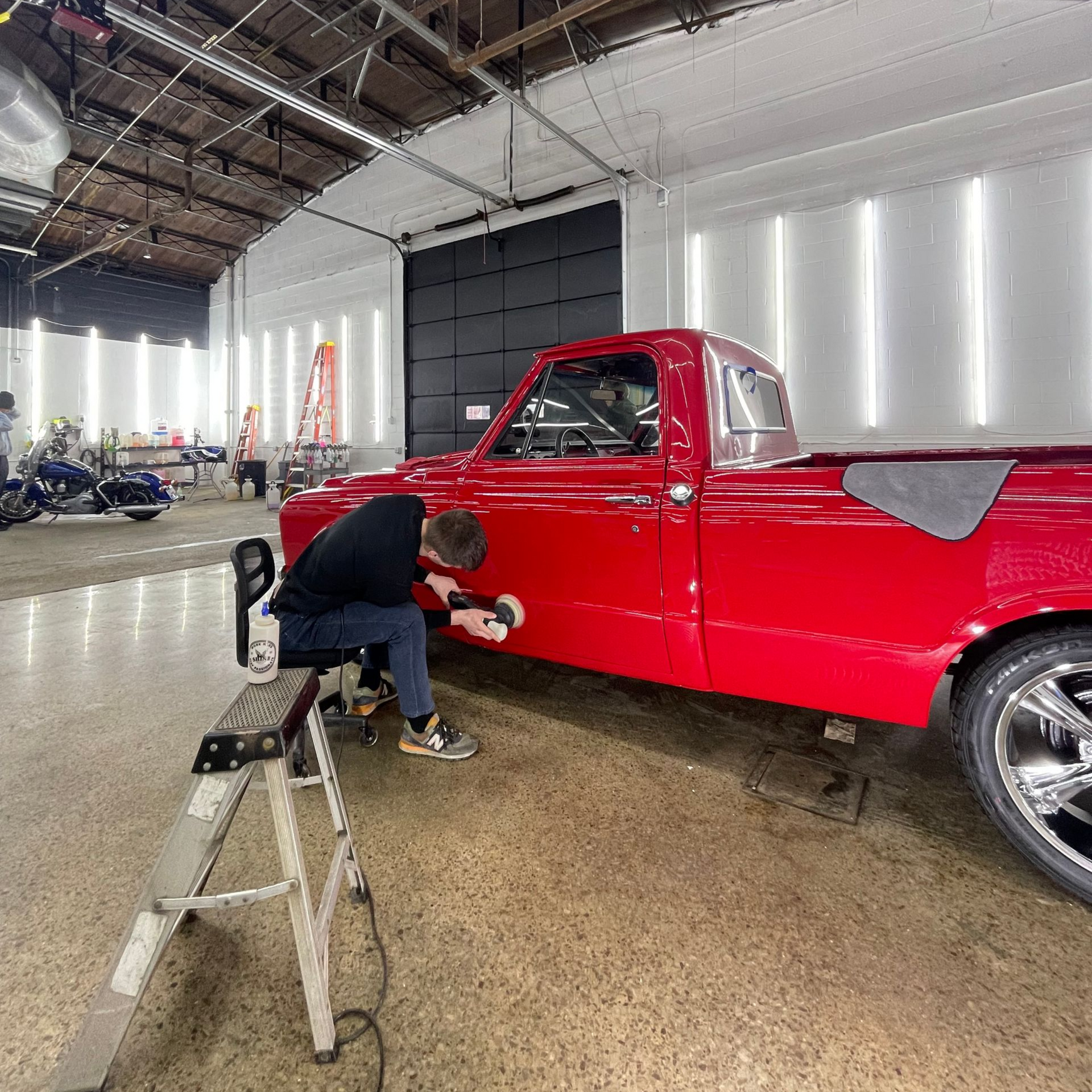Person polishing a red pickup truck inside a garage