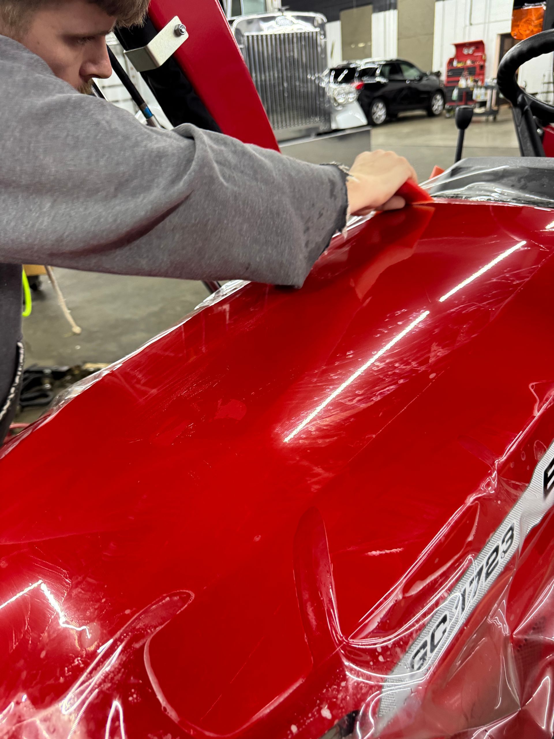 Worker polishing a glossy red car body in an auto shop