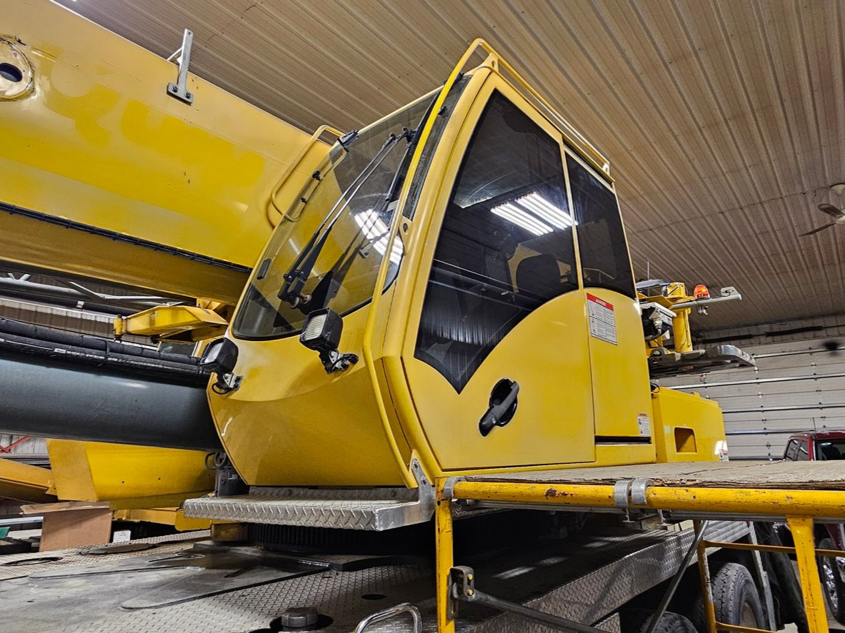 Yellow industrial crane cab indoors at a maintenance facility, with large equipment nearby