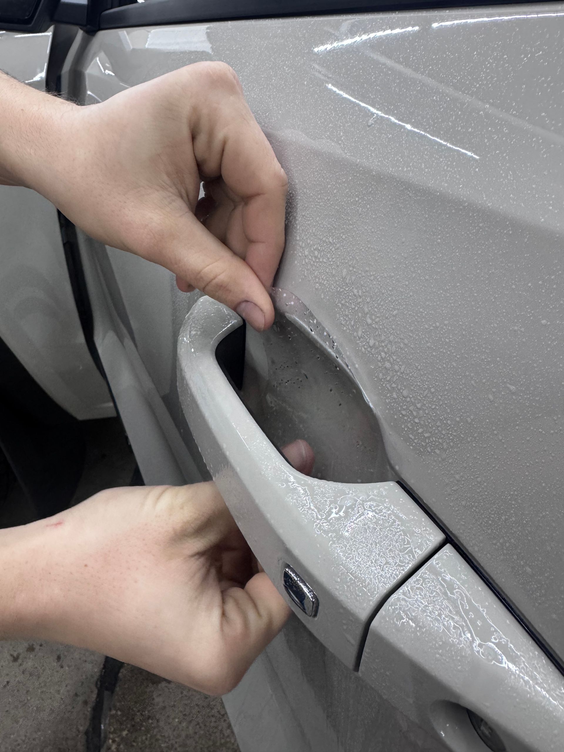 Hands opening a silver car’s exterior door handle to show the recessed grip.