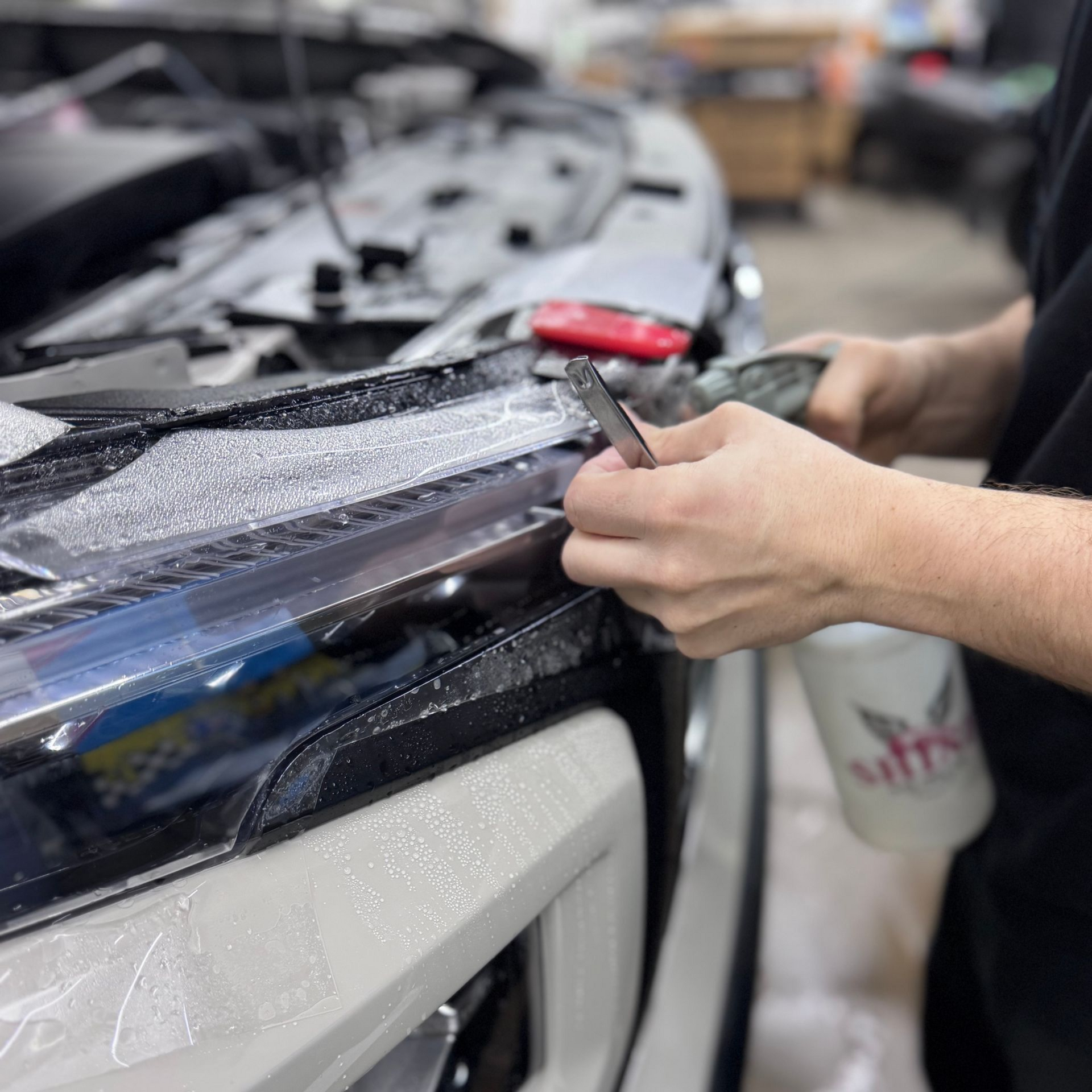 Person applying clear protective film to a car hood in an auto workshop