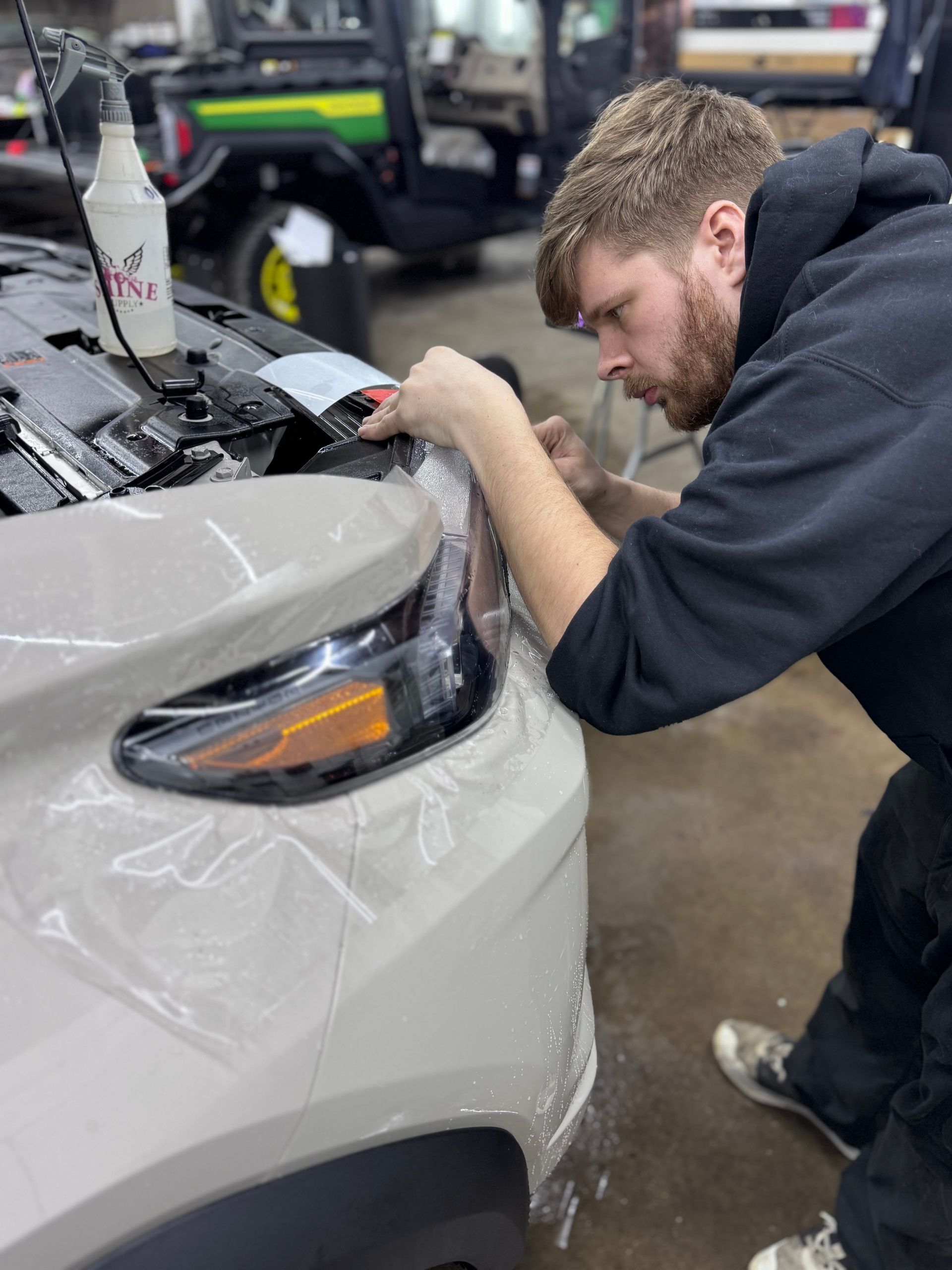 Mechanic applying clear film to the front fender of a white car in a garage