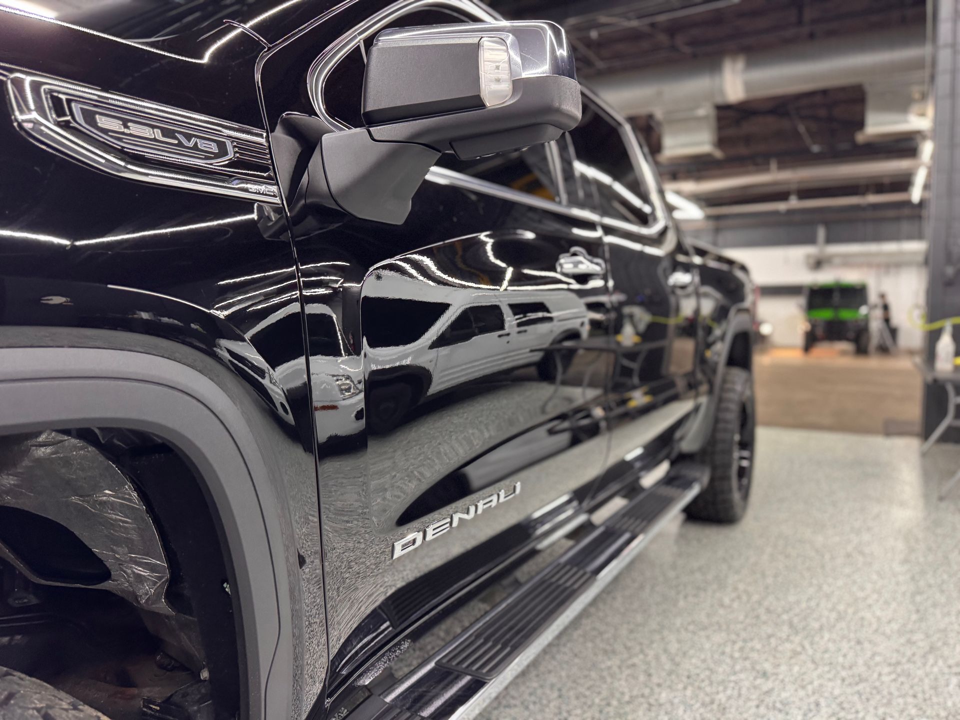 Black pickup truck in a garage, shown from the side with glossy reflections and off-road trim.