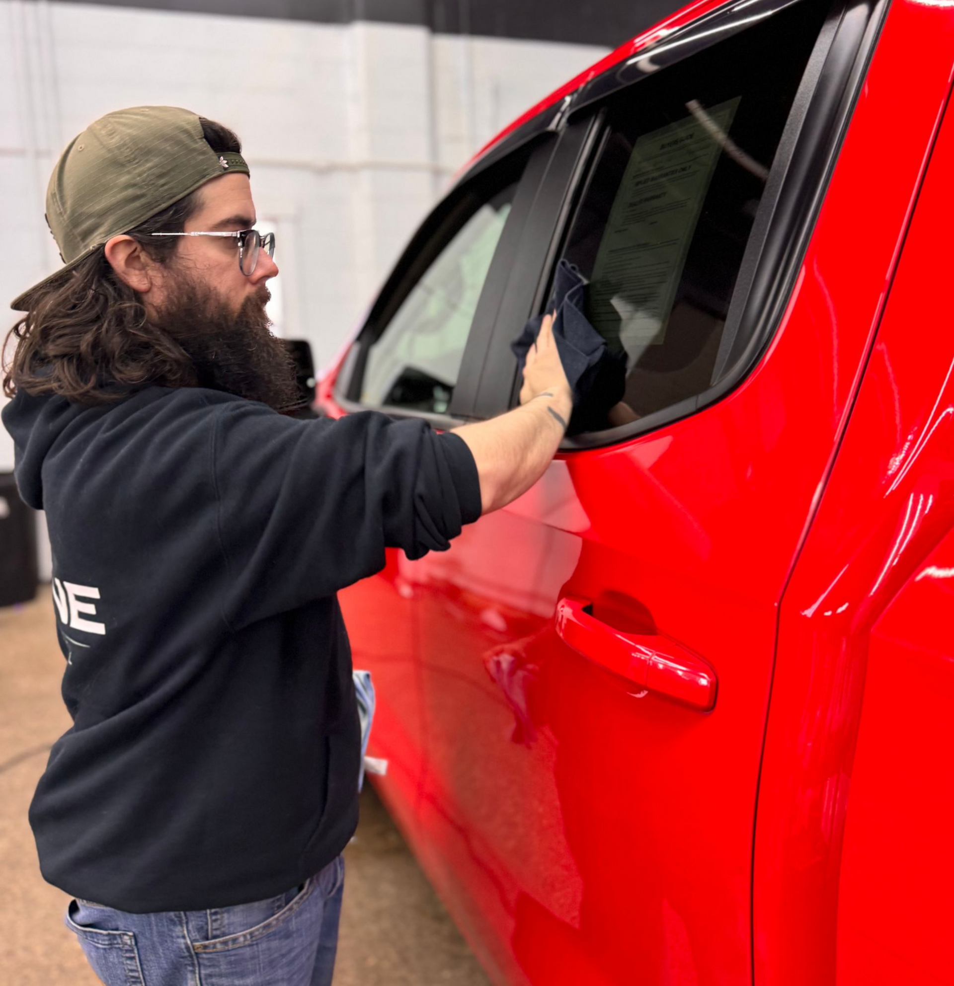 Man applying window film to a red car in a workshop
