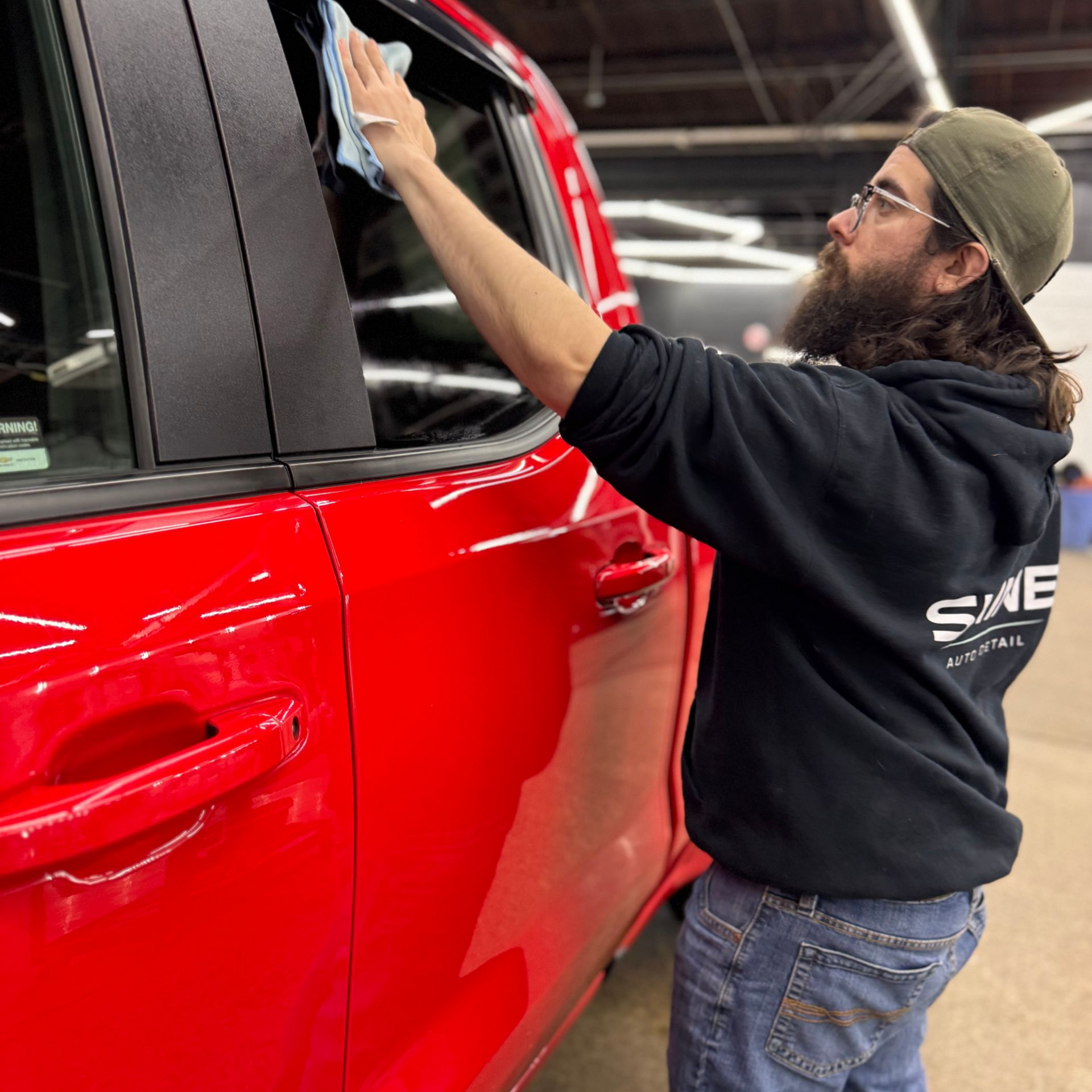 Person wiping the window of a red car inside a garage