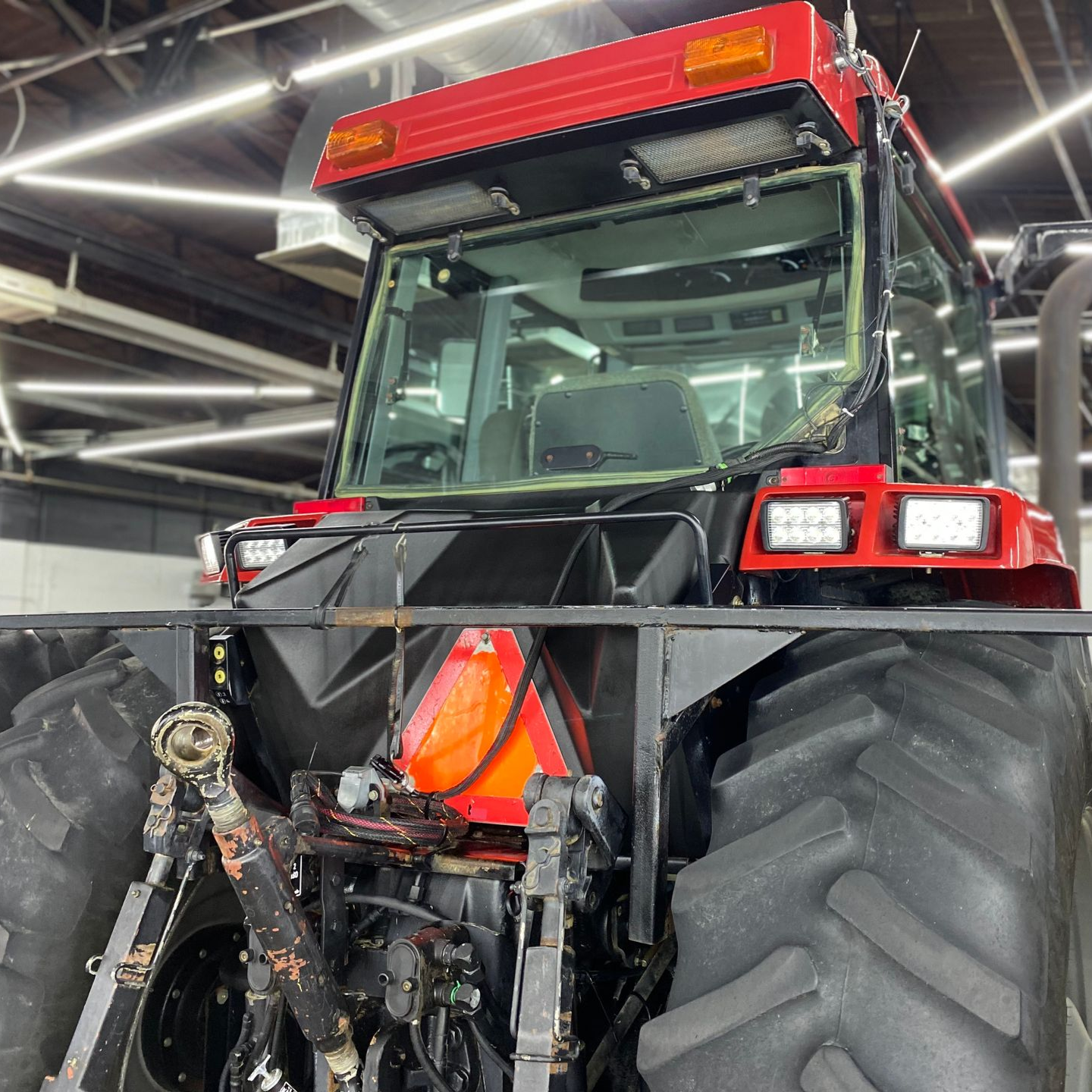 Red tractor with front attachment in a garage, under bright overhead lights.