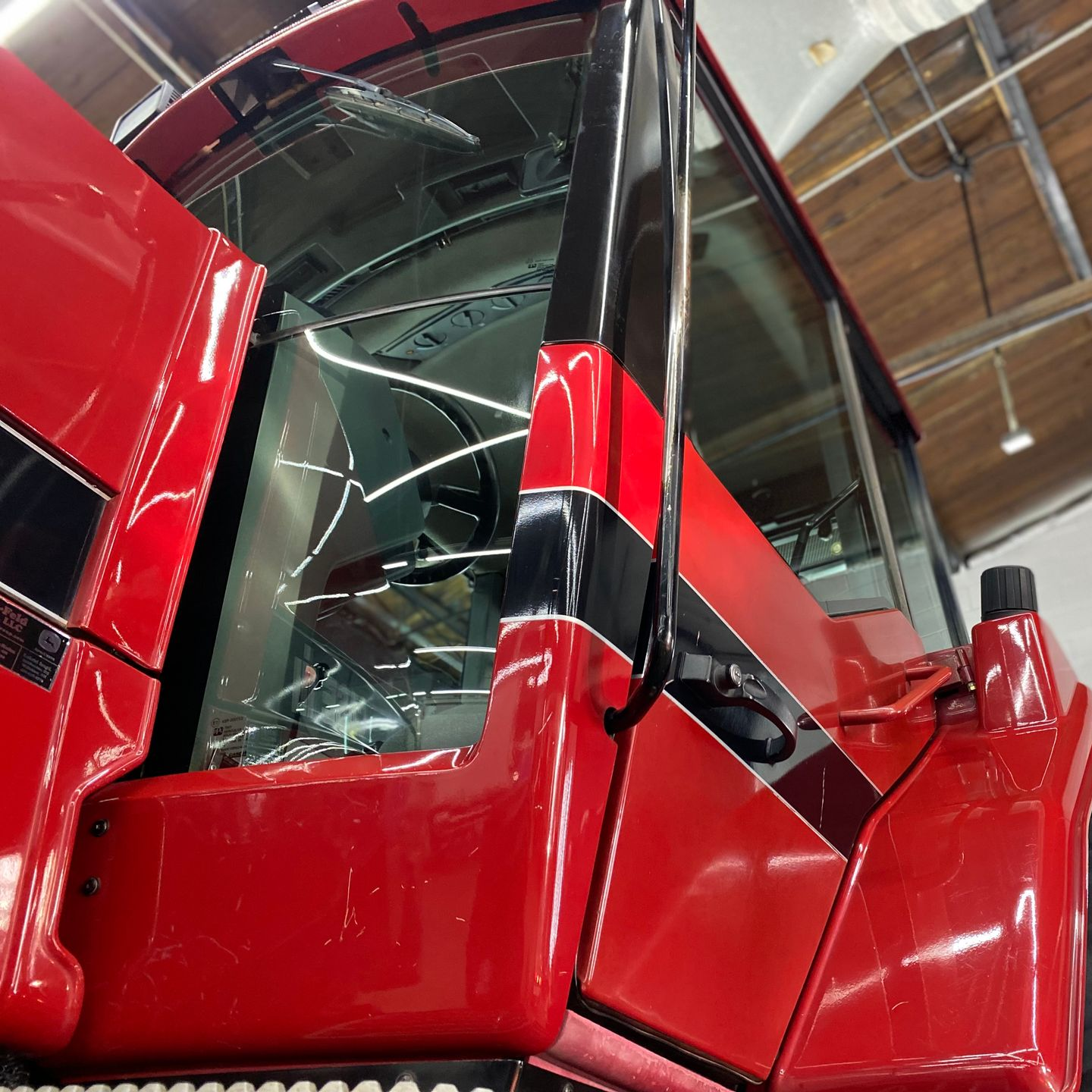 Close-up of a glossy red truck cab with black trim and side mirror in a warehouse
