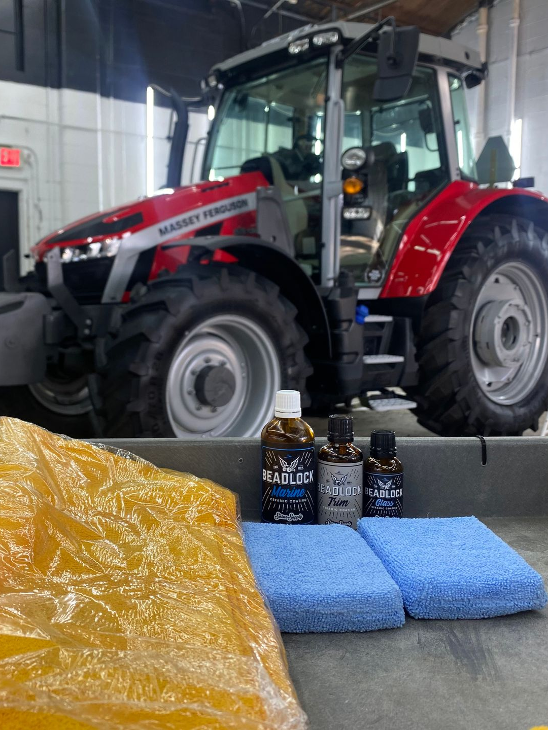 Red tractor in a garage behind cleaning supplies, blue microfiber cloths, and spray bottles