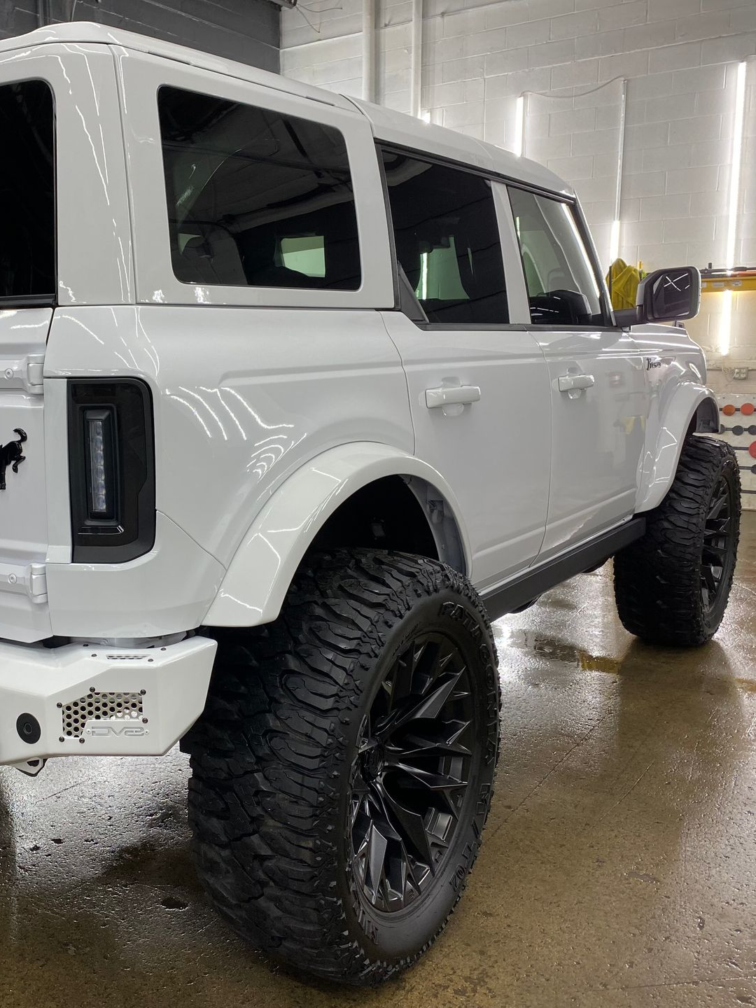 White lifted SUV with oversized black tires parked indoors on a wet floor