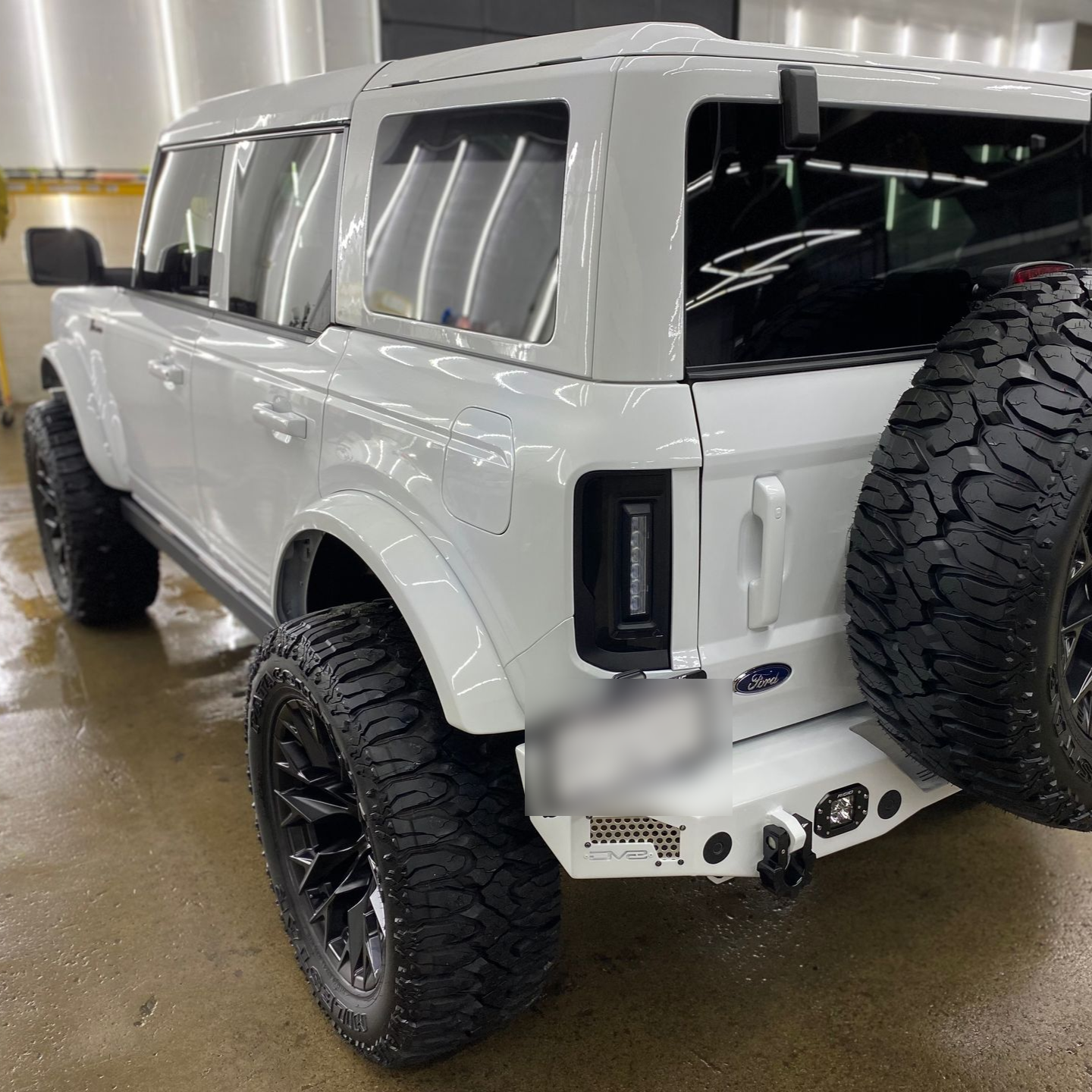 White off-road SUV with black wheels and spare tire parked indoors on a wet floor