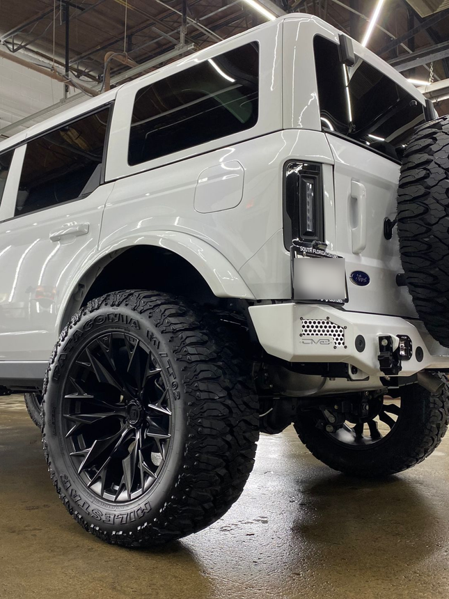 White lifted off-road SUV with oversized black wheels in a garage, viewed from the front side.