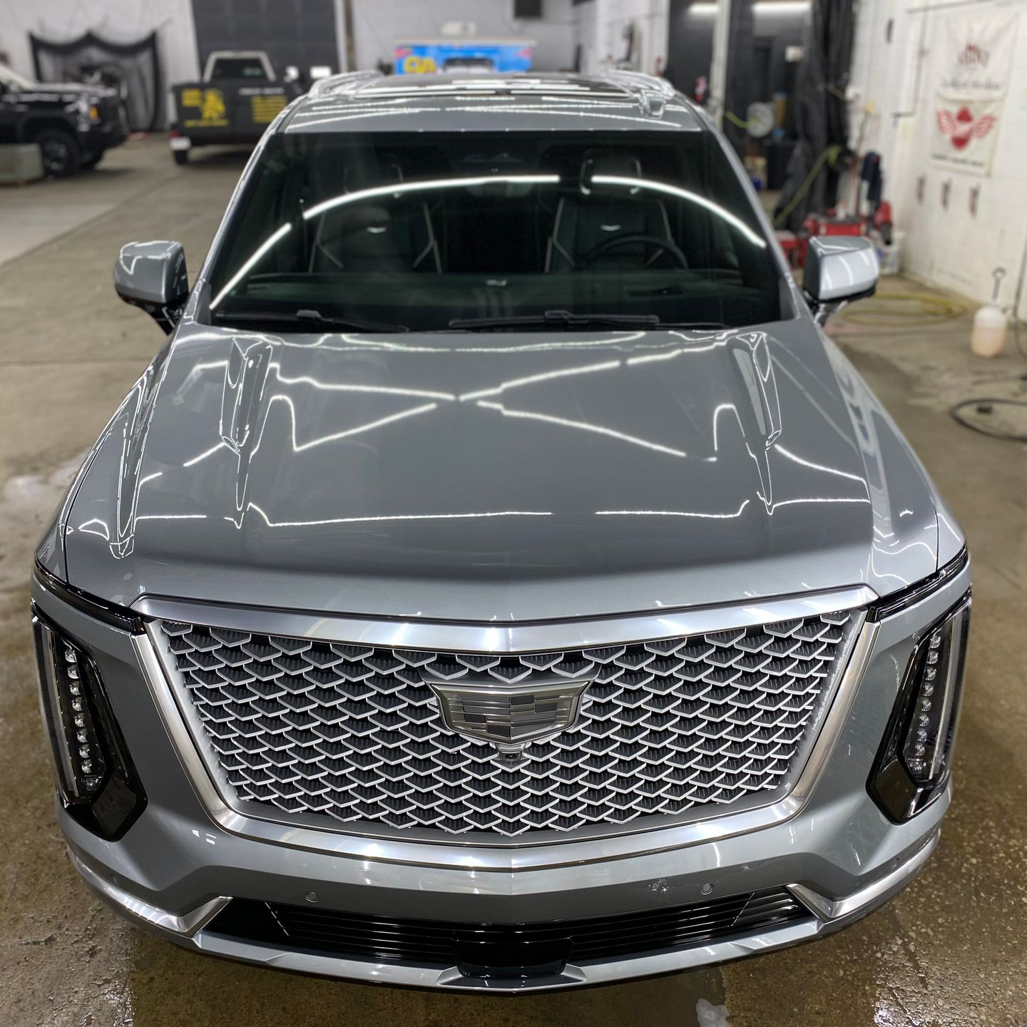 Gray Cadillac SUV in a garage, front view with chrome grille and headlights.