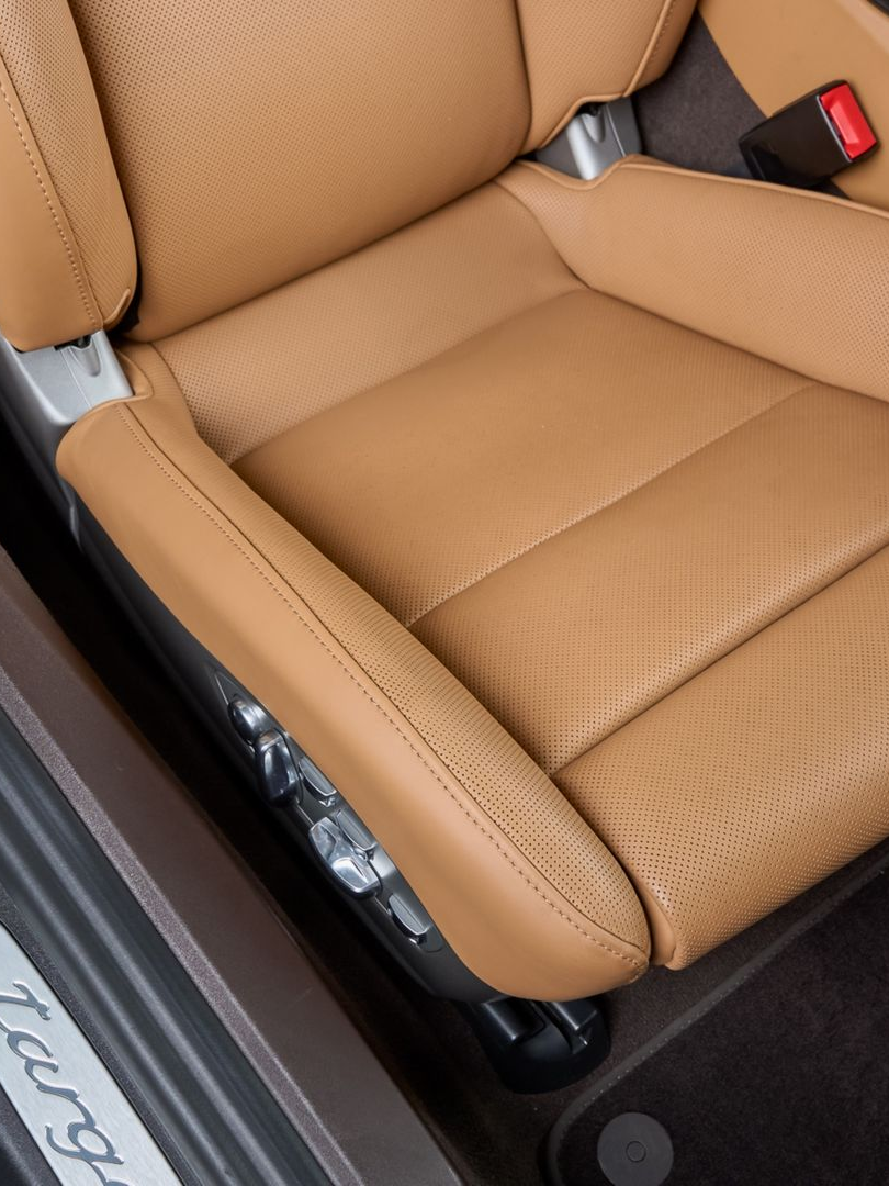 Tan leather car seat with perforated cushion and black interior trim, seen from the open door