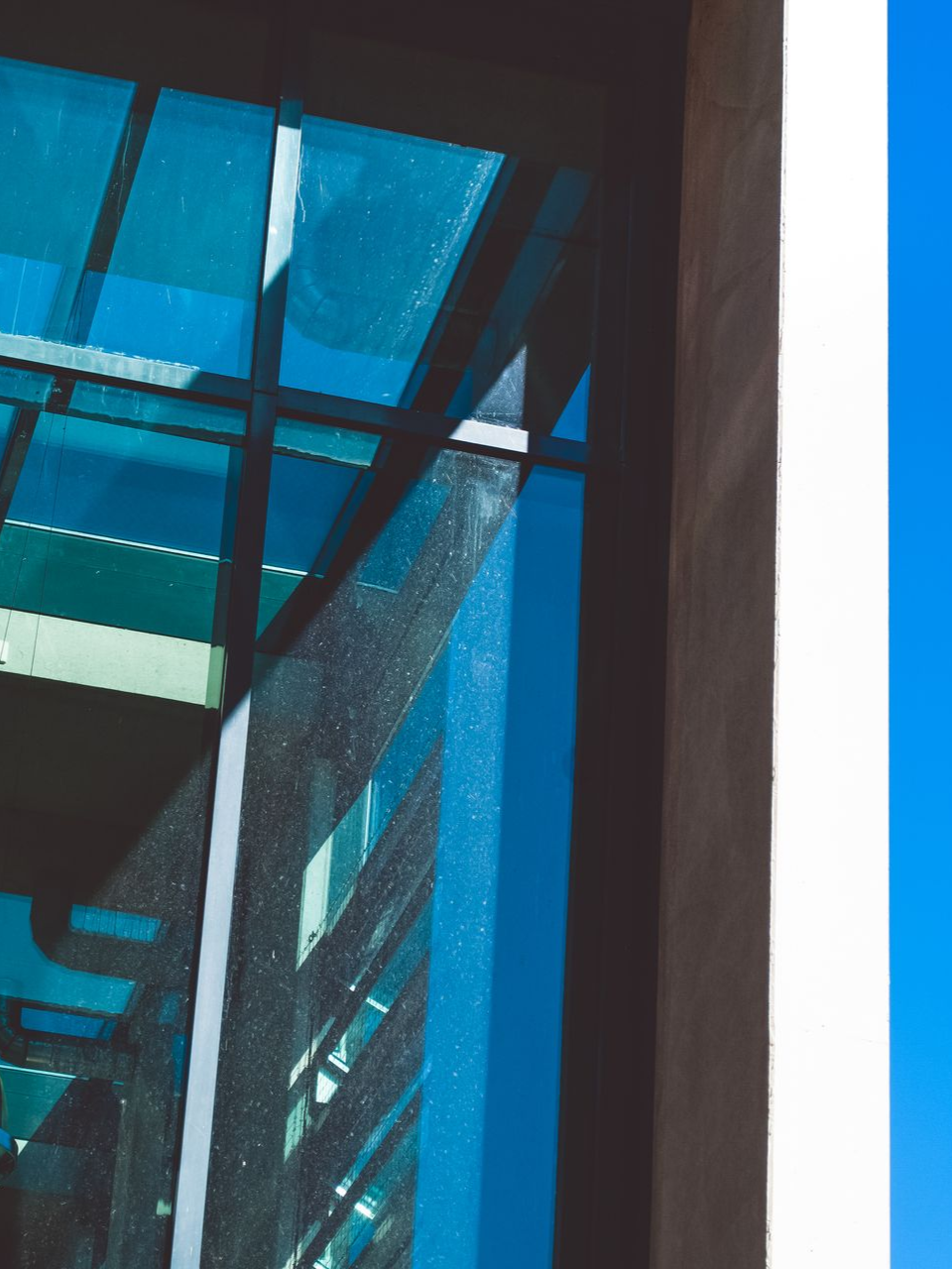 Blue glass atrium with steel beams and sunlight streaming through the windows