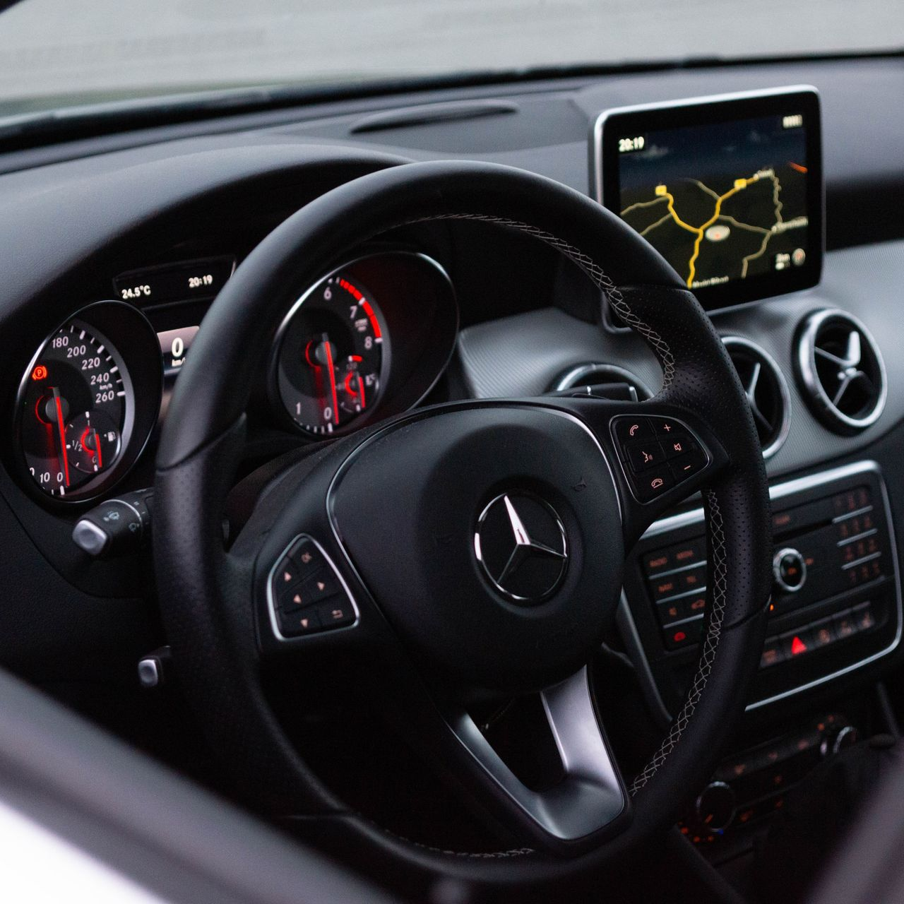 Mercedes-Benz car interior with steering wheel, dashboard gauges, and navigation screen