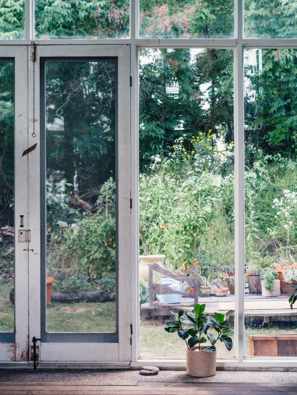 Glass doors opening onto a lush garden, with potted plants on the patio and a small plant indoors.