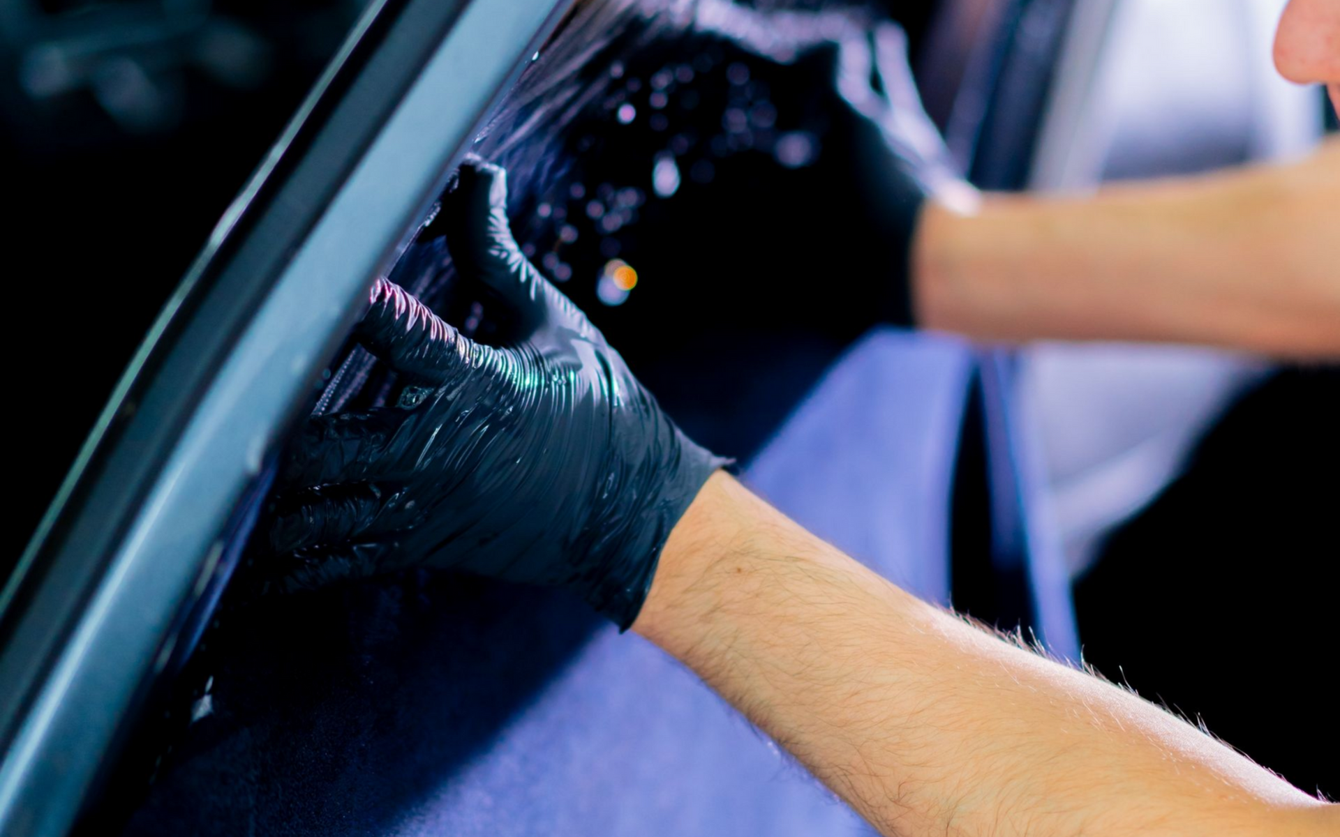 Gloved hands washing a car window with soap and water