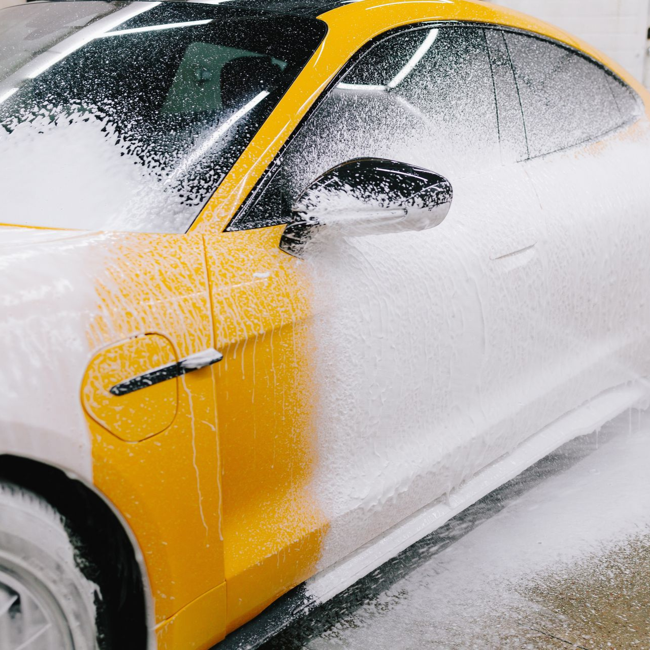 Yellow car being sprayed with white foam in a car wash