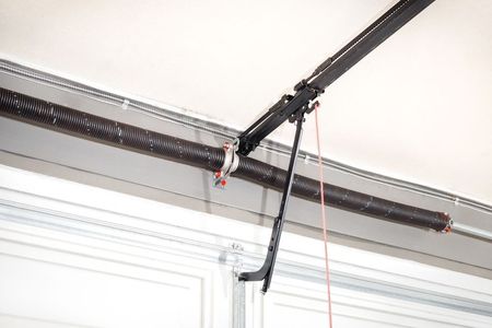A close-up of a garage door opener motor rail and a metal arm attached to a white door panel with a red emergency rope.