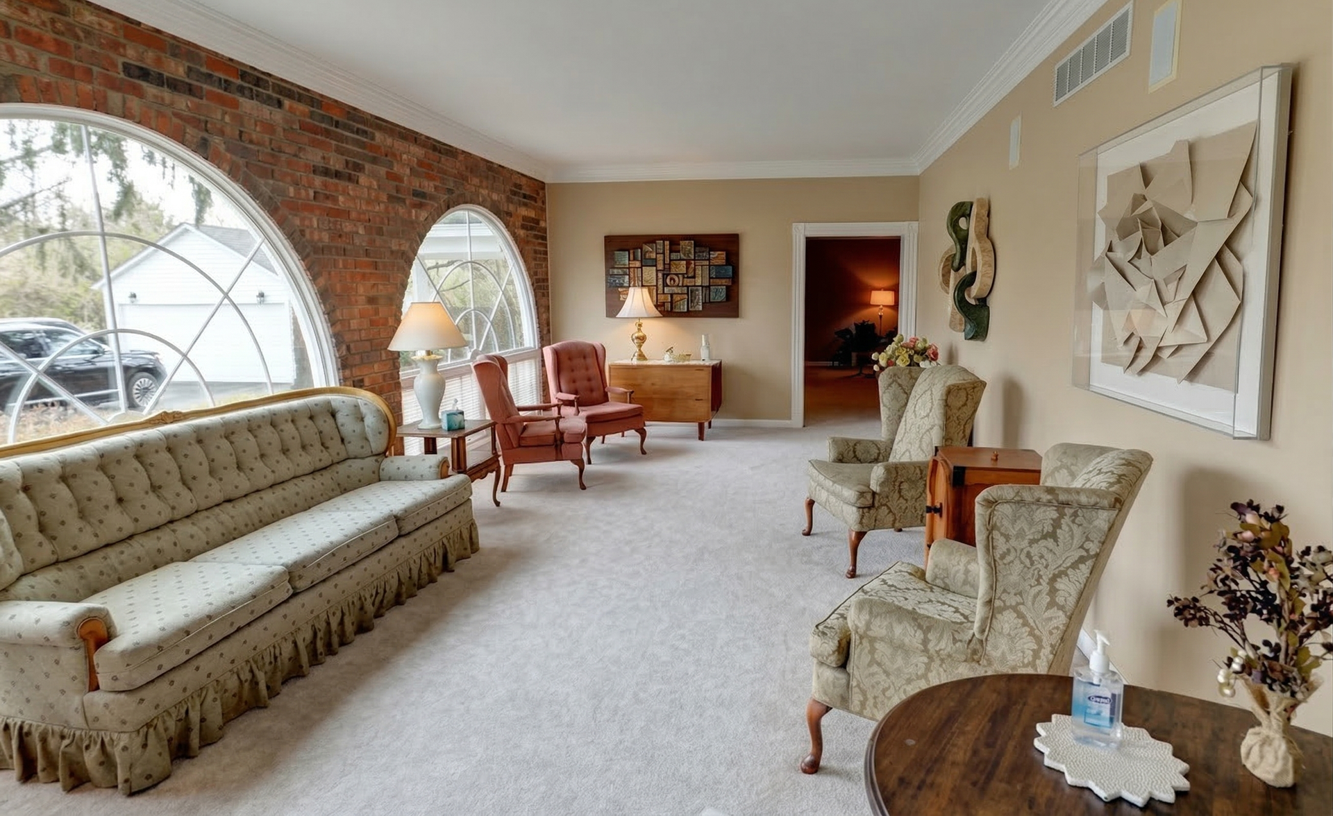 Bright living room with arched windows, beige sofa, patterned chairs, and warm brick walls