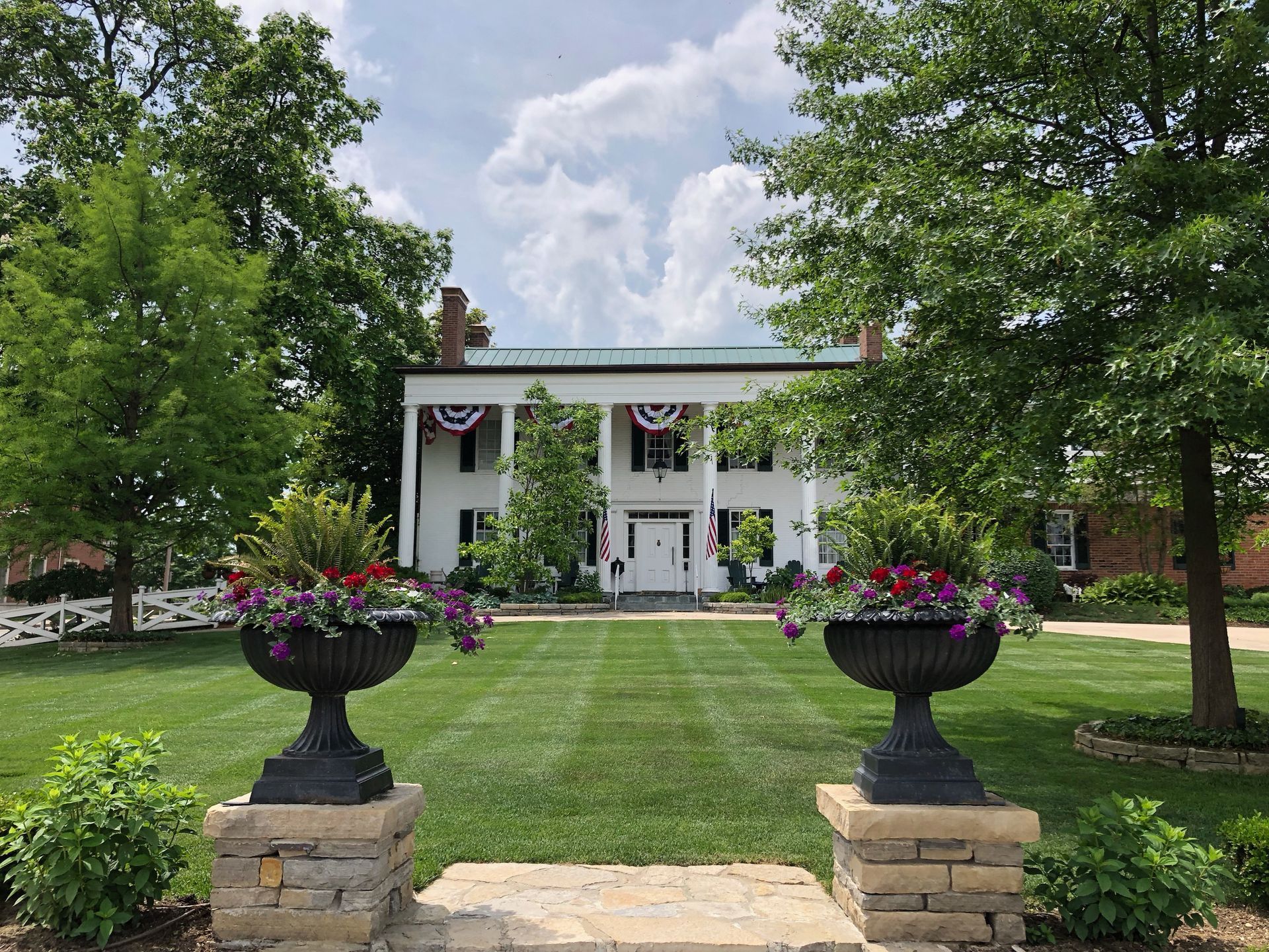 White house with columns and manicured lawn framed by flower urns and trees