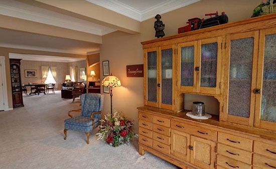 A furnished living room features a wooden hutch, a blue armchair, and a floor lamp, with a dining area visible beyond.