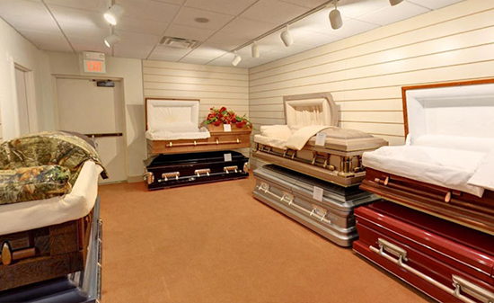 A showroom displaying several open and closed caskets in various colors and finishes on carpeted flooring.