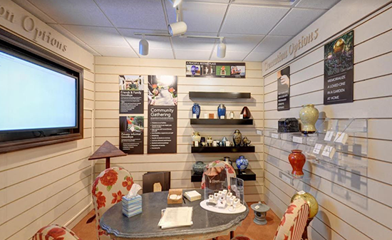 A consultation room featuring a table, chairs, wall-mounted display shelves with urns, and a television screen.