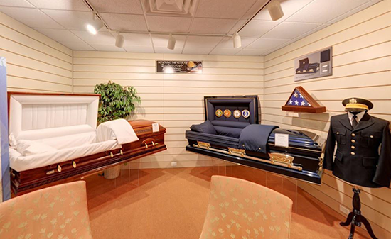 A showroom displaying two caskets, one featuring military insignias, with a folded flag and a formal uniform on a stand.
