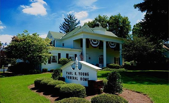 The white Paul R. Young Funeral Home building with columns and decorative bunting, set in a green lawn with shrubs.
