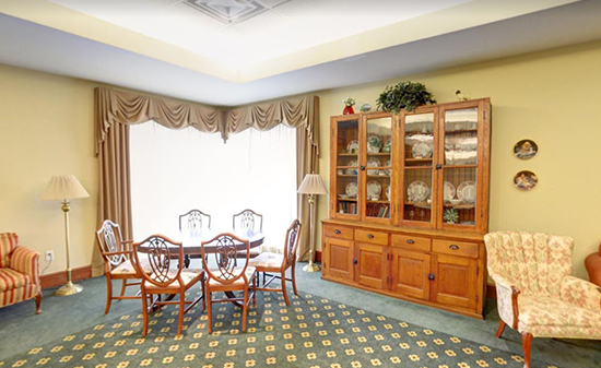 A dining area with a round table, four chairs, a large wooden hutch, and two armchairs on a patterned carpet.
