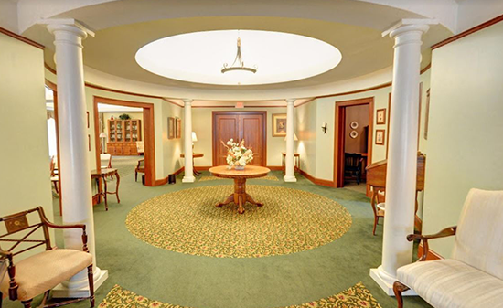 A circular hotel lobby with a central table, green carpet, white columns, and light green walls.