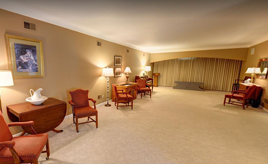 Spacious, neutrally-toned waiting room with several red armchairs, tables, lamps, and floor-to-ceiling curtains.