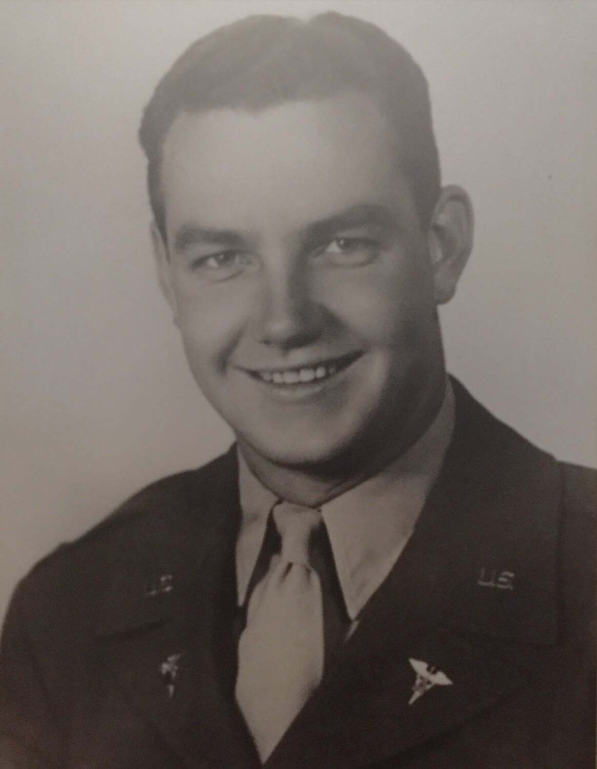 A black-and-white portrait of a smiling person in a military uniform with Medical Corps insignia on their collar.