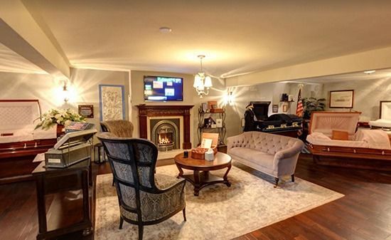 A funeral home display room featuring a fireplace, seating area, and multiple open caskets on wooden pedestals.