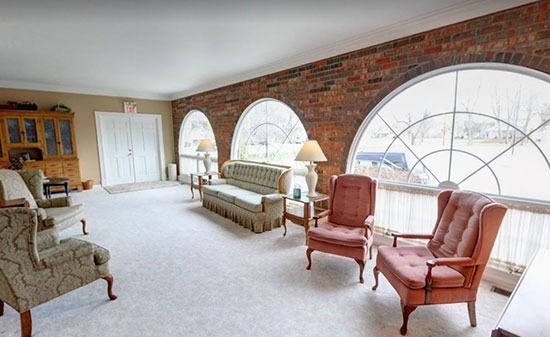 A seating area with a brick wall, three large arched windows, a sofa, and four armchairs on a light-colored carpet.