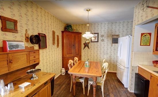A rustic dining room with patterned wallpaper, a wooden table and chairs, a large corner cabinet, and a white refrigerator.