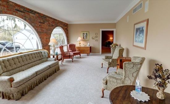 A spacious, beige waiting room with a brick accent wall, large arched windows, a sofa, and several armchairs.