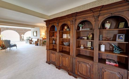 A large wooden bookshelf with four arched sections stands in a bright room, looking toward an open living area.