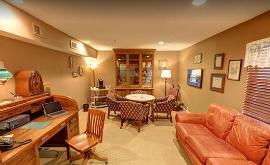 A cozy office featuring a wooden desk, a leather sofa, and a small table with chairs, set against warm beige walls.