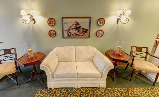 A seating area with a light-colored sofa, two wooden side tables, and two matching chairs against a pale green wall.